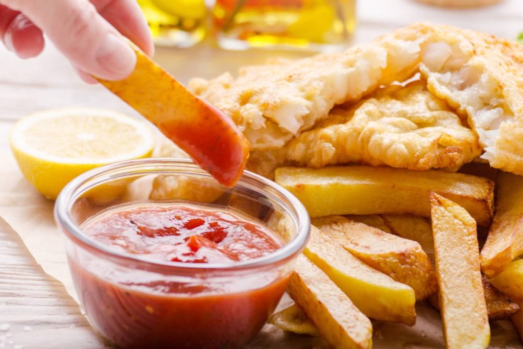 Traditional British street food fish and chips with ketchup sauce and lemon on bakery paper