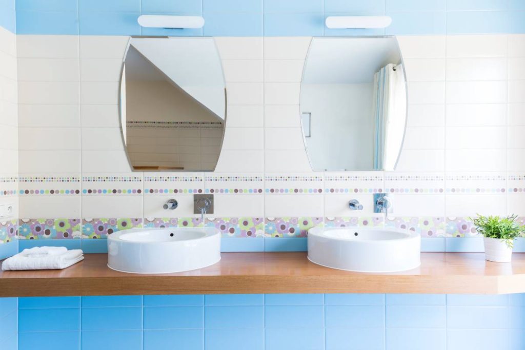 Two oval sinks with mirrors in the minimalist bathroom with blue tiles