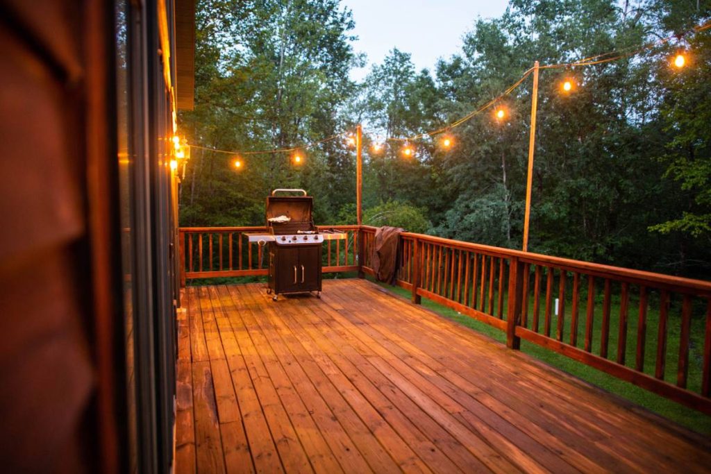 A wooden porch with string lights and grill