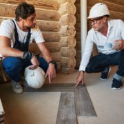 Housebuilder and construction specialist squatting near pieces of parquet while discussing the correct way to install it
