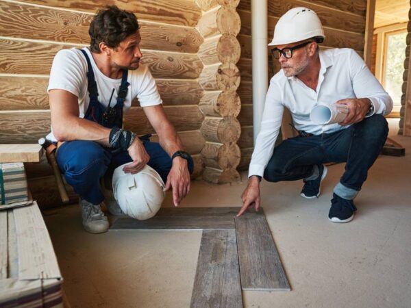 Housebuilder and construction specialist squatting near pieces of parquet while discussing the correct way to install it